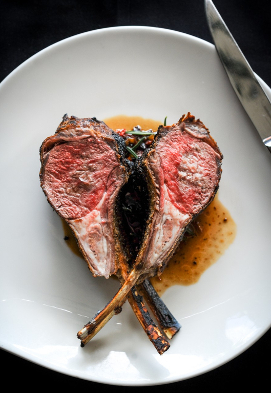 Two grilled lamb chops with pink center on white plate with sauce, crossed bones forming heart shape